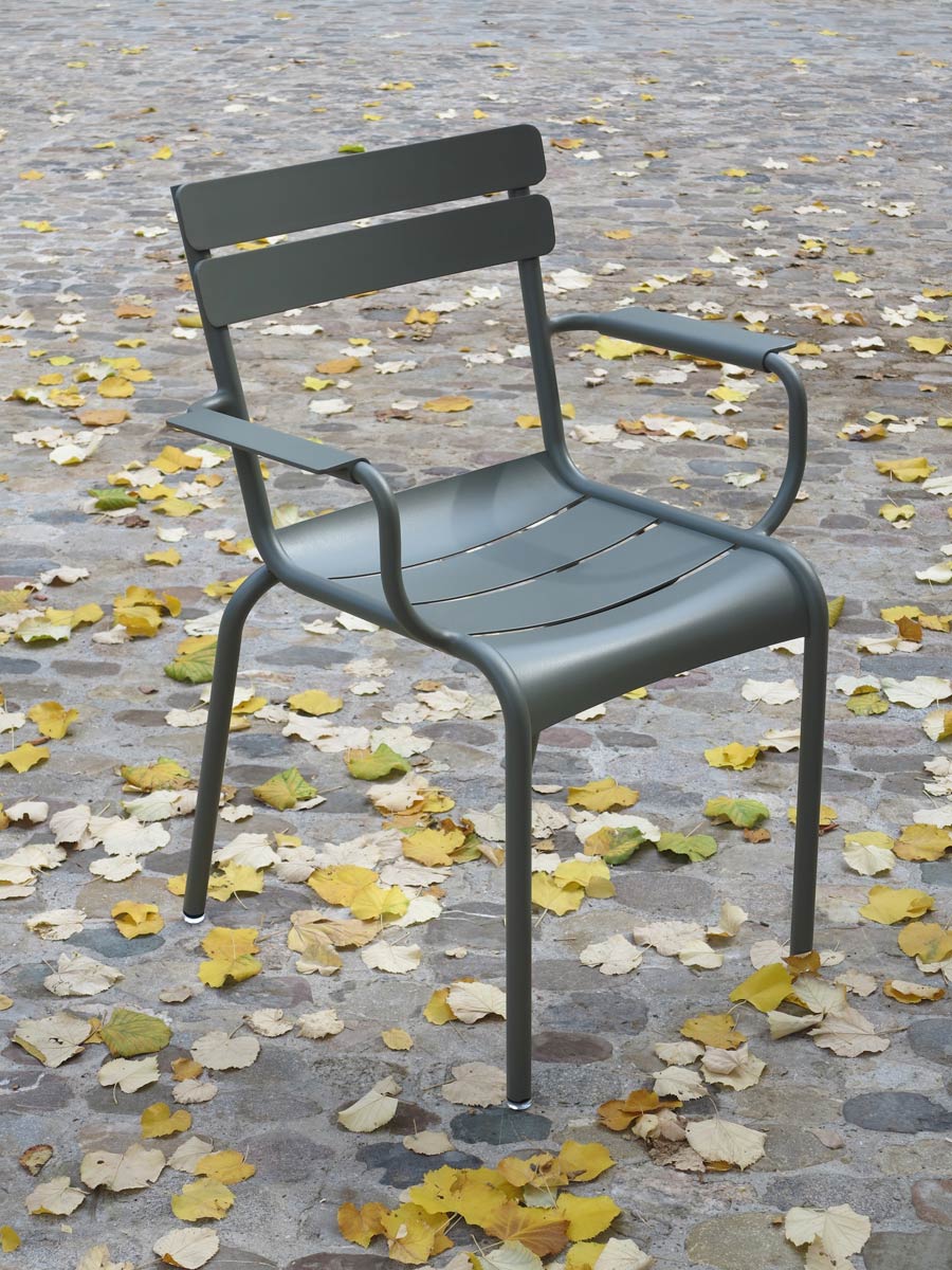 Fermob «Luxembourg» Gartenstuhl mit Armlehnen auf Kopfsteinpflaster mit gelben Gingko-Blättern im Herbst