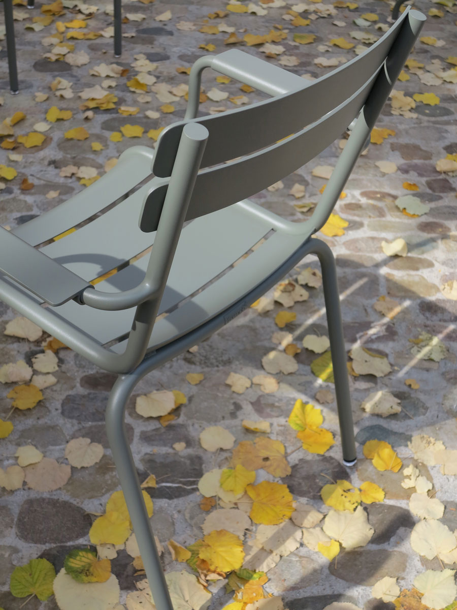 Fermob «Luxembourg» Gartenstuhl mit Armlehnen auf Kopfsteinpflaster mit gelben Gingko-Blättern im Herbst