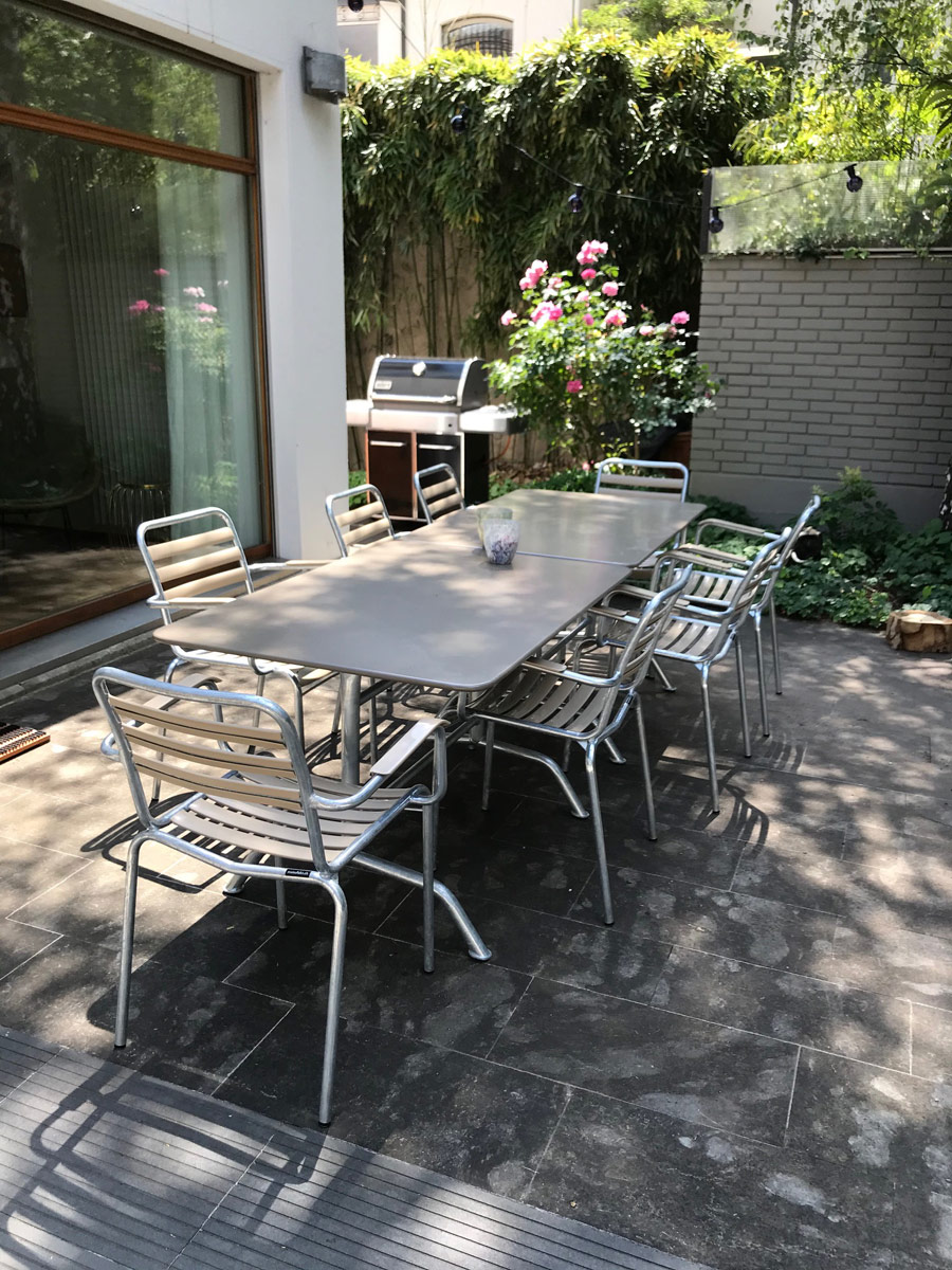 Hinterhof mit zwei Bättig Gartentischen in Schlammgrau und acht Bättig Gartenstühlen in Beige