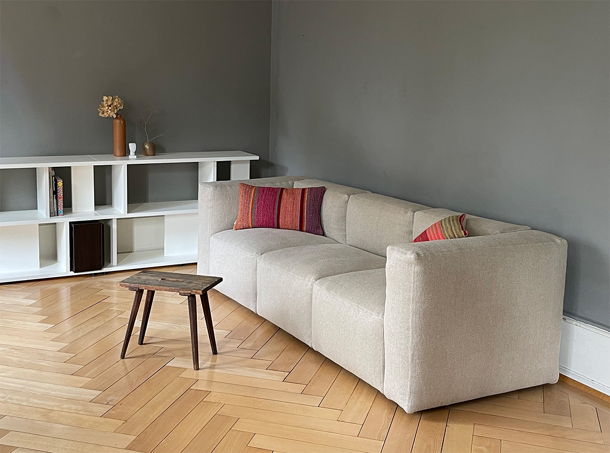 Cubell Sofa mit Leinenbezug in Beige, roten Kissen, vor einer dunkelgrauen Wand