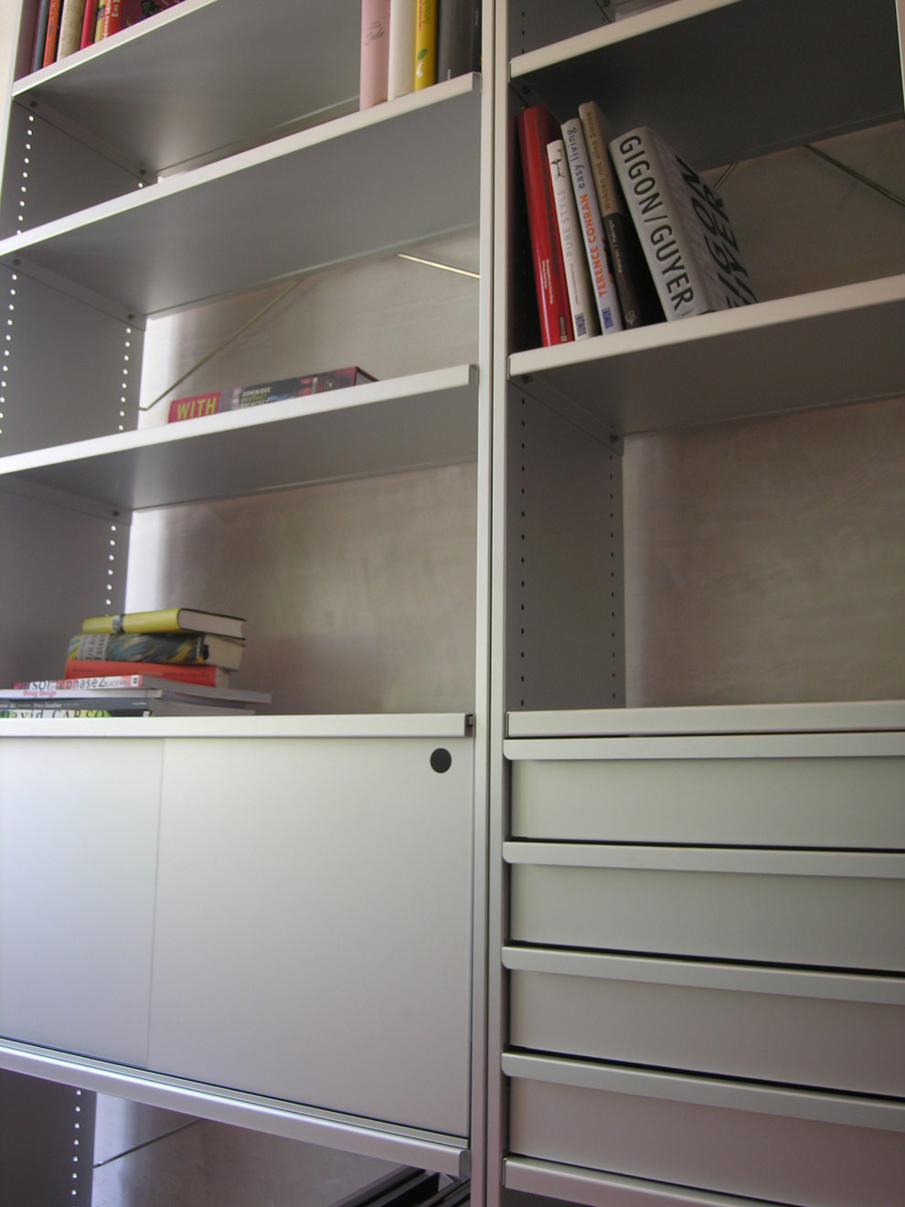 Detailaufnahme von Lehni Regal vor Betonwand auf rotem Boden mit einzelnen Büchern